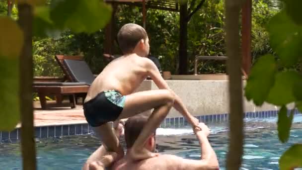 Muž drží malého chlapce nad hlavou skočit do bazénu