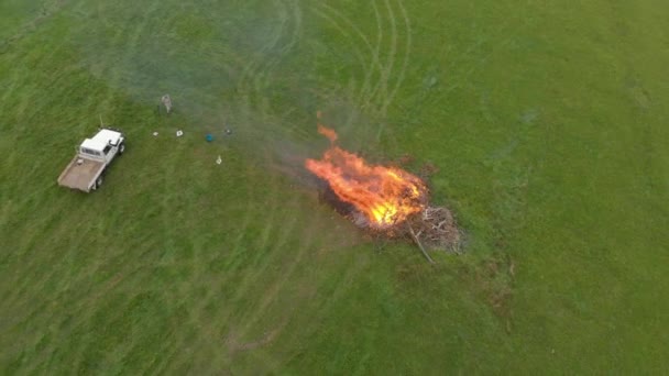 空飛ぶ鳥の目のビューは 農場のパドックに大きなたき火で農家や彼のトラックの上を飛んで撮影 — ストック動画