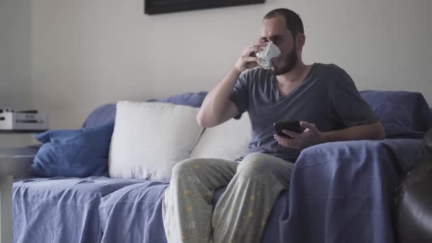 家で働く前にソファで朝一番のコーヒーを飲んでる男 — ストック動画