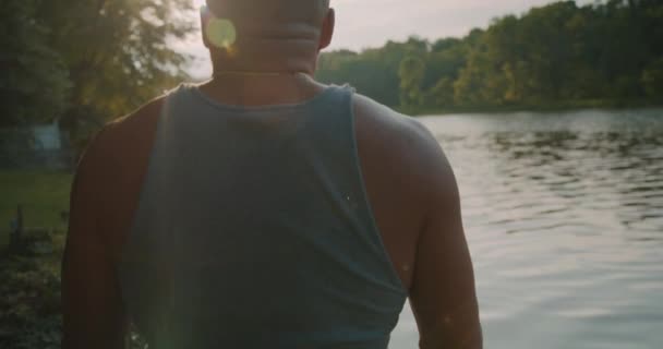 光秃秃的 棕褐色的 肌肉发达的男人站在那里 用太阳耀斑看着外面的小溪 — 图库视频影像