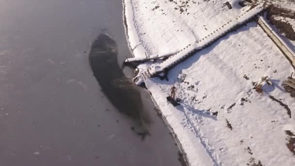 凍った湖の岸近くにドローンが降下し 氷の水泳の後にタオルを使用して乾燥させる 氷の水と雪に覆われた風景の中にスカンジナビアの極性急落 — ストック動画