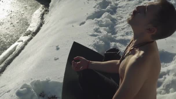 Muž sedící na černé jógové rohoži ve sněhu bez košile těžce oddechuje, aby připravil mysl a tělo na mrazivý pád do zamrzlého horského jezera. Slunce na košili bez chlapa hyperventilace před extrémním sportem.