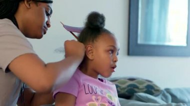 Afro-Amerikalı bir kızın evde otururken saçını ördürdüğü orta boy bir fotoğraf..