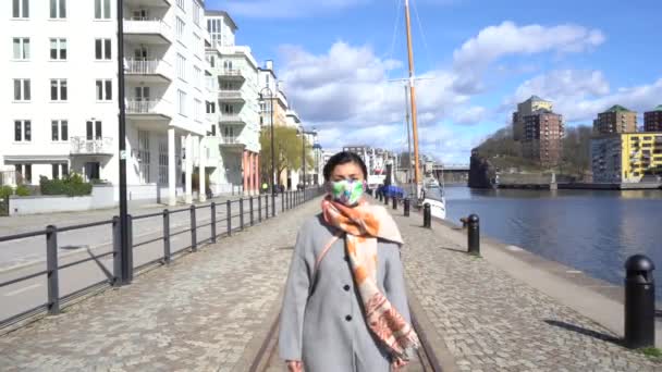 Asijská dívka je chůze v ulici u moře a ona má na sobě ochrannou bezpečnostní masku proti coronavirus nouzové. Modré moře v pozadí. Švédsko, Stockholm, ochrana proti virům, zůstat zdravý