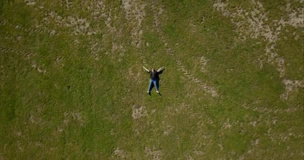 一名身穿黑色T恤衫的成年女子躺在公园的绿草上 空中无人驾驶飞机从她上方飞过 — 图库视频影像