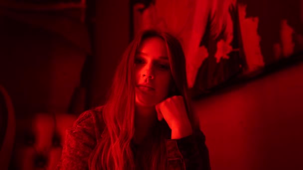 Female with long hair sitting in a bar with red neon lighting looking at the camera. Blurred and close up