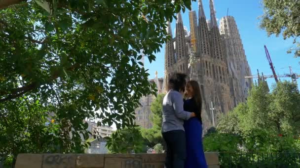 バルセロナの有名なサグラダ ファミリア大聖堂を背景に 公園で晴れた日に若いカップルが踊ってキスをします — ストック動画