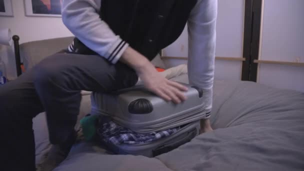 Young Man Sits His Overloaded Travel Suitcase Trying Close Both — Stock Video