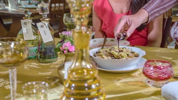 黄金のテーブルクロスとカラフルなガラスとテーブルの上に伝統的なレストランでスロベニア料理の上にソースを注ぐ男 パンニングショット — ストック動画