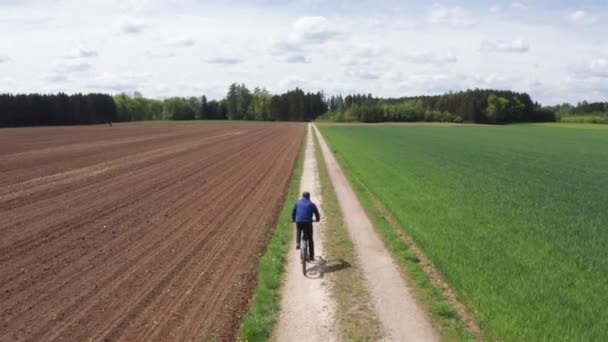 晴れた日には真っ直ぐな未舗装の道を自転車に乗っている男 自転車に乗るの空中ワイドショット — ストック動画