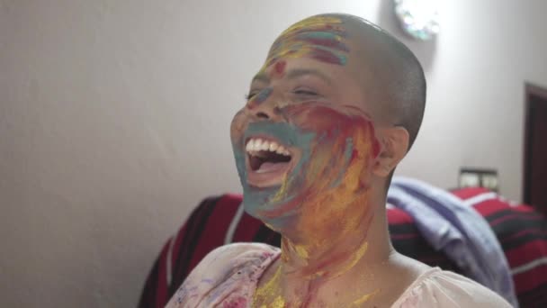 Happy and hopeful cancer patient bald girl applies colored powder on cheeks at home on Holi and laughs