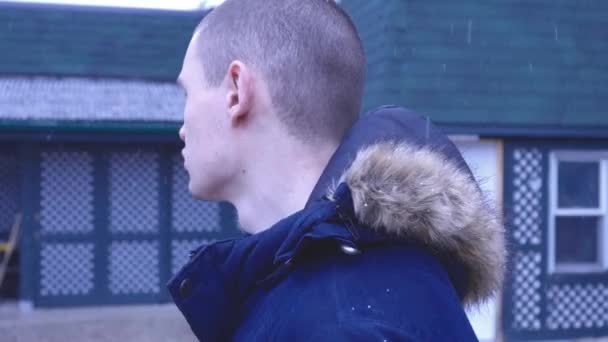 カナダで雪が降っているのを見ながら家の外に立つ冬のコートを着た男 閉じるショット — ストック動画