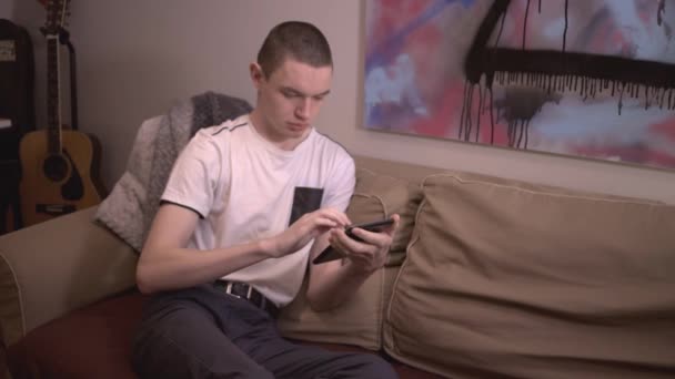 Νεαρός Που Κάθεται Στον Καναπέ Κρατώντας Και Κυλιόμενος Στην Ηλεκτρονική — Αρχείο Βίντεο