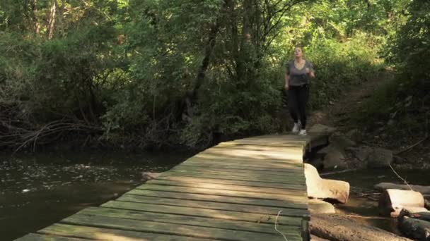 在森林中央一条小河上一座废弃的老桥上 当摄像机在右边晃来晃去时 女人们正在慢跑去 — 图库视频影像