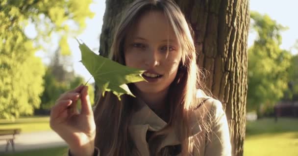 Meisje Onder Boom Met Een Gree Blad Kijkend Naar Camera — Stockvideo