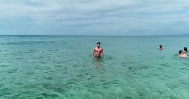 Mladý kavkazský silný atletický muž v plavkách kráčející v průzračné mořské vodě v zamračený den, stoupající vzad