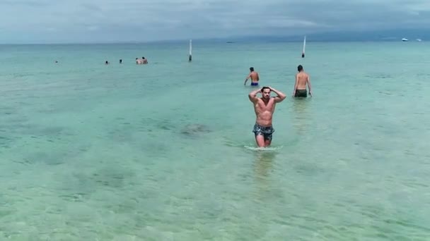若い白人男性運動選手と強い男水着を着て海岸に向かって澄んだ海の水の中を歩くショートパンツ スローモーション — ストック動画
