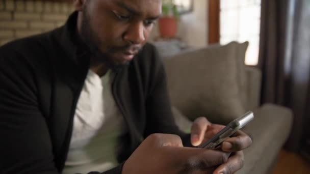 Fekete férfi sms-ezés telefon koncentrátumok a nappaliban közelről dönthető