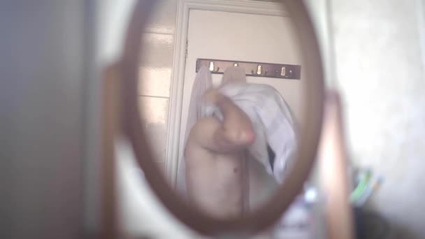 Mladý muž si obléká košili v koupelně, zrcadlo v popředí, statický výstřel
