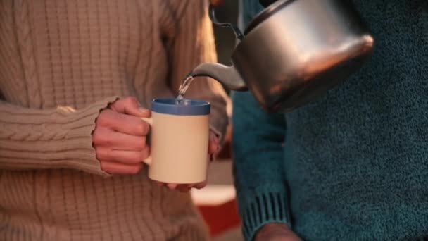 Close up; Man pours hot steaming water from teapot to mug held by woman; sunny outdoors