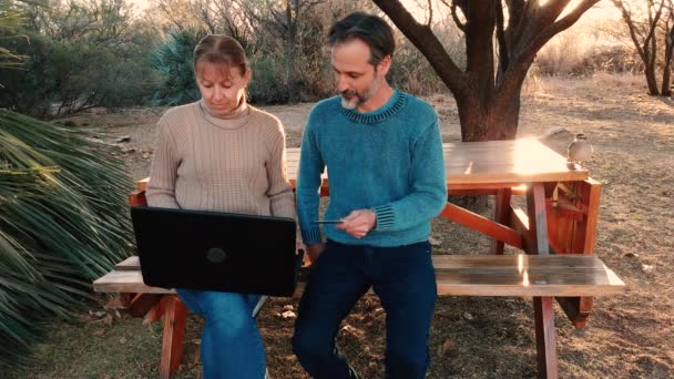 Starý pár dělat on-line platby na notebook; sedí na dvorku / parku; příjemné počasí