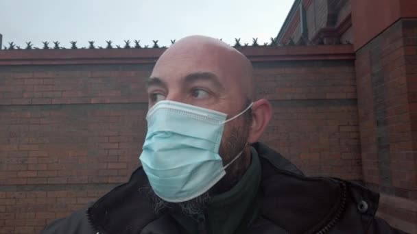Muž bezpečnostní stráž opravuje ochranné korona virus lékařské PPE masky před vysokou cihlovou zdí