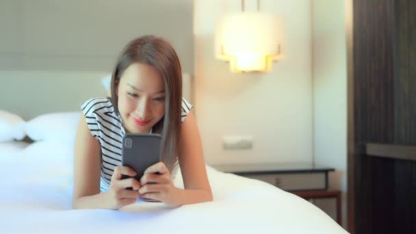 ベッドのスマートフォンでテキストを入力します 携帯電話でチャットベッドルームで若い幸せなアジアの女性 スローモーション 選択的フォーカス — ストック動画