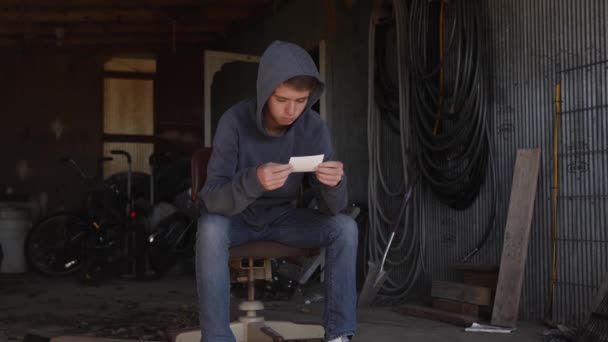 Nastoletni Chłopak Siedzi Sam Brudnym Garażu Patrzy Zdjęcie Strzał Zwolnionym — Wideo stockowe