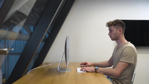 Mladý muž v profilu pracuje na PC v moderní kanceláři, příležitostné dresscode.