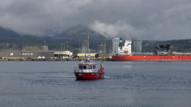 Dramatic shot of cloudscape surrounding canadian mountains and Red fire boat cruising on water in foreground.
