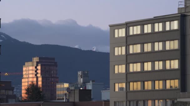 Včasný záběr zrcadlových budov ve Vancouveru a hor v pozadí. Západ slunce a soumrak večer.