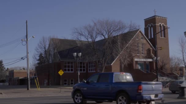 modrý pickup odjíždí vlevo na klidné křižovatce, kde není nikdo venku na to, co je typický rušný víkend se starou ranou 1900s církevní budovou na obzoru a středovou značkou NO EXIT