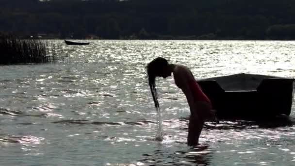 年轻的女人慢吞吞地把湿透了的头发扔回来 头发上的水会飞溅 日落时的湖景 — 图库视频影像