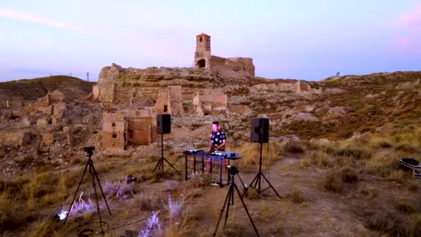 Disc Jockey Playing and Mixing Records the Sunset. Orbital drone view over the Dj and forward there is a ruined castle.
