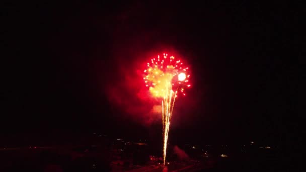 Fireworks bright vibrant colorful finale ending exploding going off in dark as drone flys backwards over lake with reflections in water, with final shooting star at the end. In 4k 30fps.