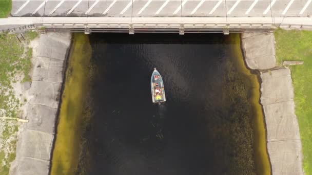 在阴天 一架自上而下的无人驾驶飞机从运河中的一条船上飞过 摄像机往下看 像娃娃似的跟着船 车辆在立交桥上驶过 云彩反射在水面上 — 图库视频影像
