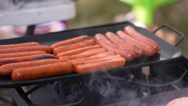 Hot dogy hovězí maso vepřové a zeleninové klobásy vegetariánská rostlina na bázi vaření na litinové pánvi gril v kempu, těsný výstřel s kouřem fouká ve větru. Ve 4k 30fps zpomalil z 60fps.