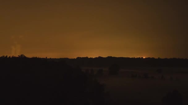 Smoke rising over horizon with glowing golden sky and fog rolling on ground, timelapse view