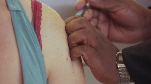 Zavřít. Ruce africké zdravotní sestry aplikují injekční stříkačku s jehlou do ramene bílé ženy v nemocnici.