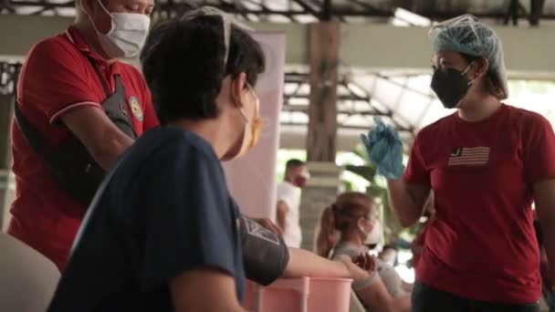 フィリピンのCovidワクチンセンターでフロントライナーによって血圧がチェックされている女性のサイドビュー ミディアムショット — ストック動画