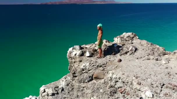 メキシコの男は夏に広い青い海を見下ろす海岸崖の上に立っています プラヤバランドラバハカリフォルニアスール メキシコで 空中ドローン軌道 — ストック動画