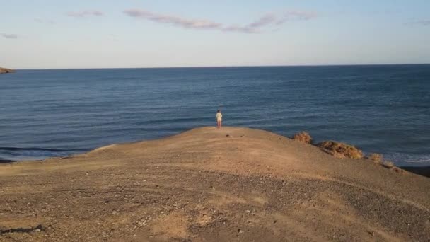 カナリア諸島 フエルテベントゥラ島の目の前の崖の上に立つ女性の空中ドローンショット — ストック動画