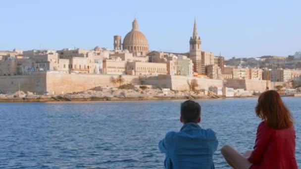 マルタの地中海の島にあるバレッタ建築の町の前の海岸線に座っているロマンチックなカップル — ストック動画