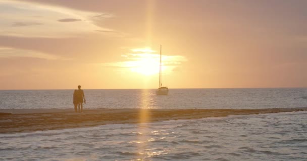 ビーチでのハッピーハニームーンカップル熱帯海とロンリーセイルボートの上の美しい夕日を見て フルフレームスローモーション — ストック動画