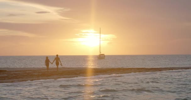 ロマンチックなカップル保持手 ビーチでのウォーキングや熱帯海と帆船の上の絵の夕日を見て フルフレームスローモーション — ストック動画