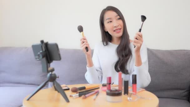A young female YouTuber films her makeup tutorial with her smartphone and tripod.