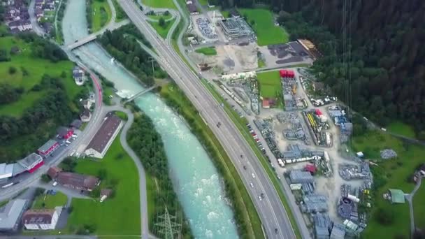 Vozidla jedoucí po silnici podél řeky a města s malebným výhledem na zelené hory v létě ve švýcarském Loganu. - letecký sklon nahoru