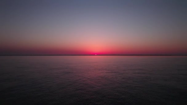 Zářící červená barva západ slunce nad klidnou mořskou vodou, vzdušný dron letící vpřed pohled