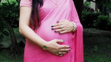 Sari giymiş hamile bir kadın çocuğuna bakarken kendini dışarıda mutlu hissediyor. Hamile karnında bebek taşıyan hamile bir anne. Doğum öncesi bakım ve kadın hamileliği konsepti.
