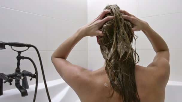 長い髪の毛に髪の毛製品を手で塗りながら 浴槽に座り心地の良い裸の女性 シャンプーなどのヘアケアで髪を洗う女性は — ストック動画